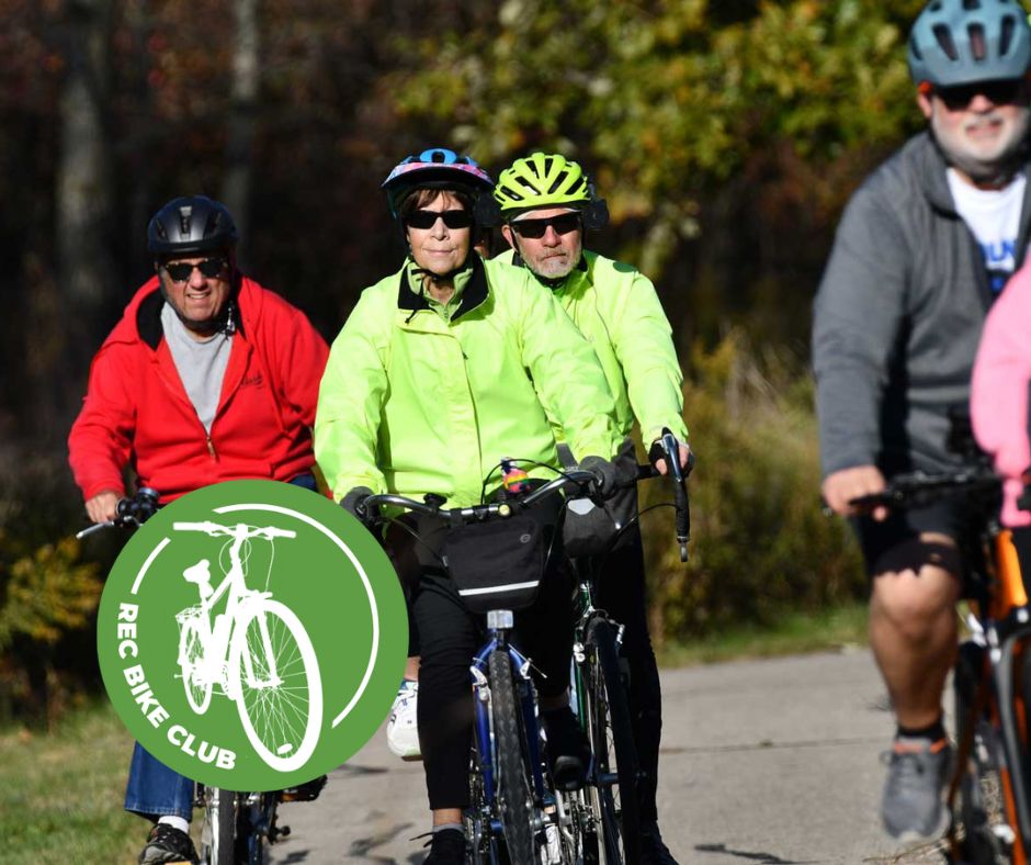 A group of people in bike helmets riding bikes on a paved trail with trees in the background.