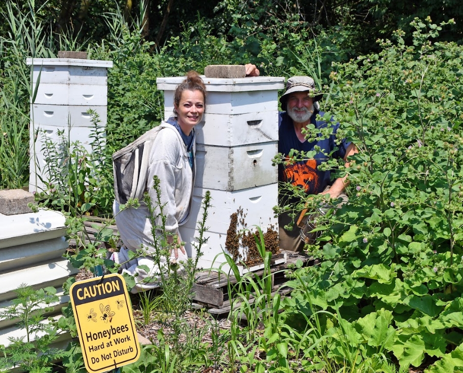 "Two beekeepers, a man and a woman, standing in front of their beehives.