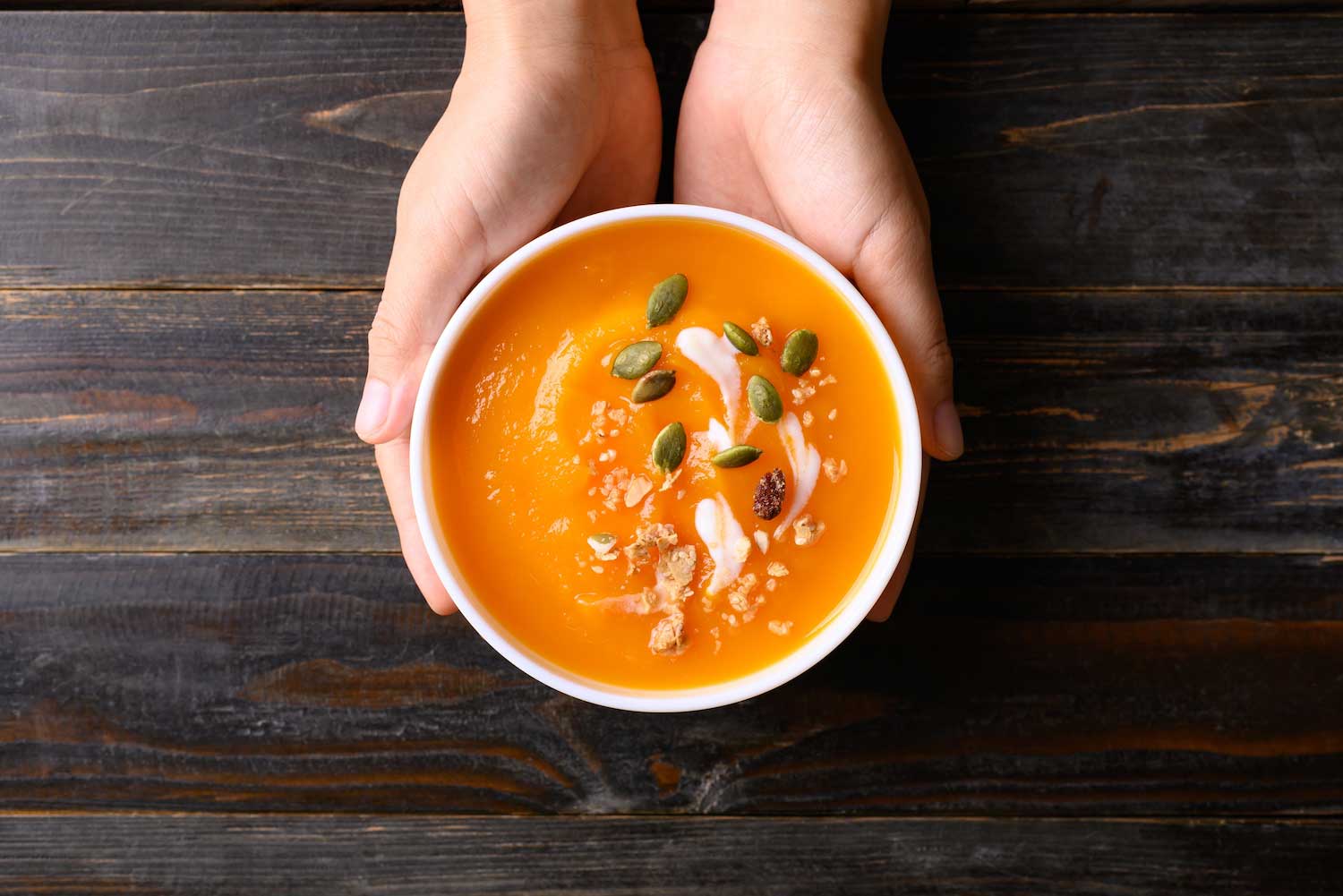 A person holding a bowl of soup over a wooden tabletop.