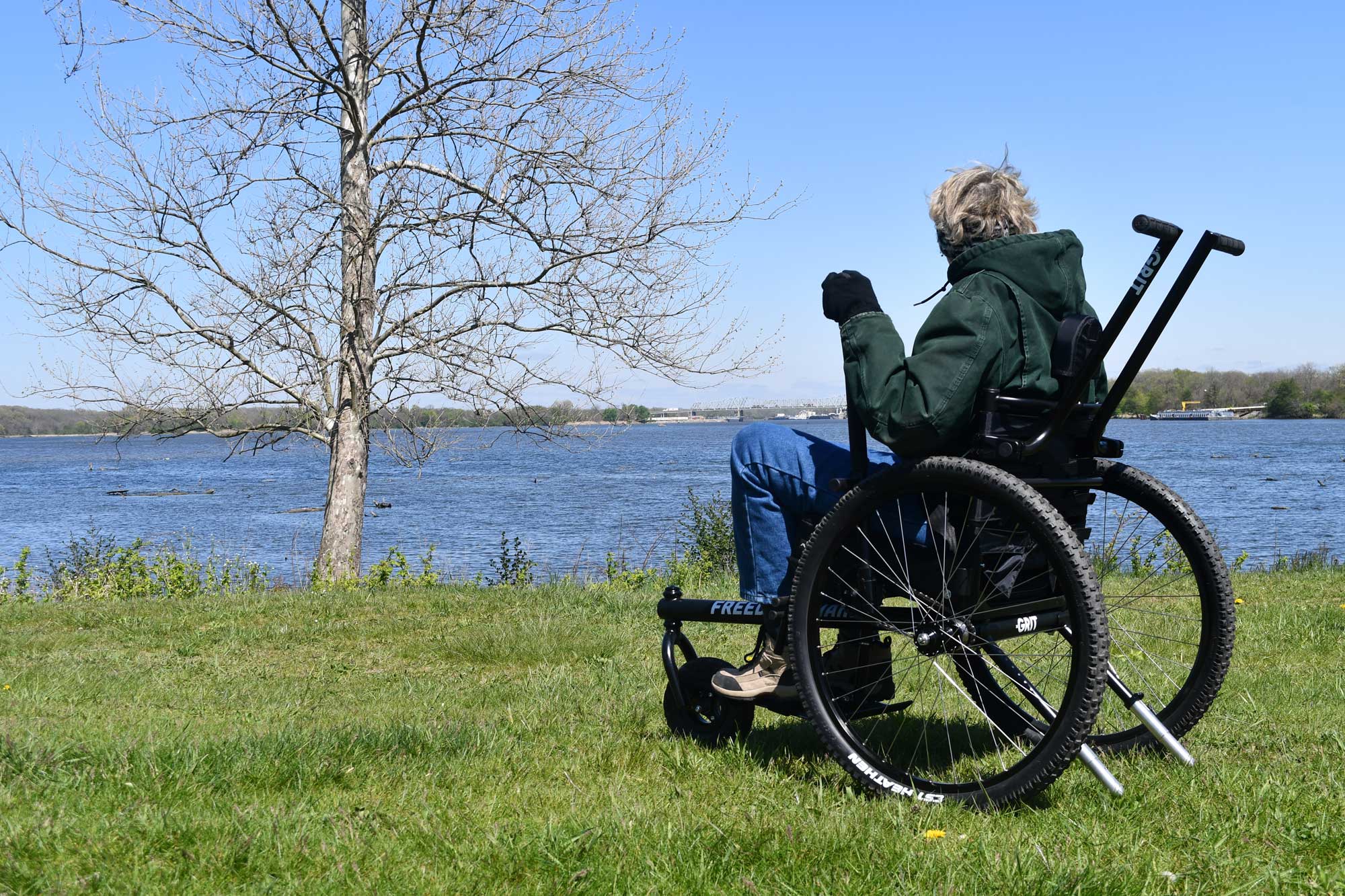 A woman in a wheelchair pauses along a river to take in the scenery.