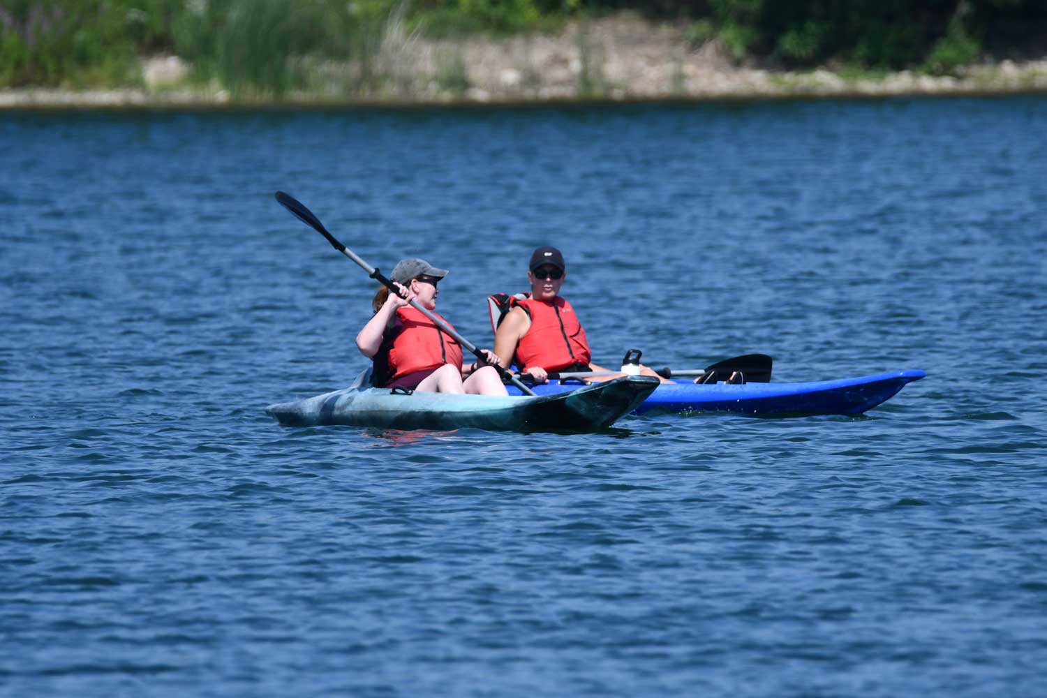 Two people side by side in their kayaks in the middle of a lake.