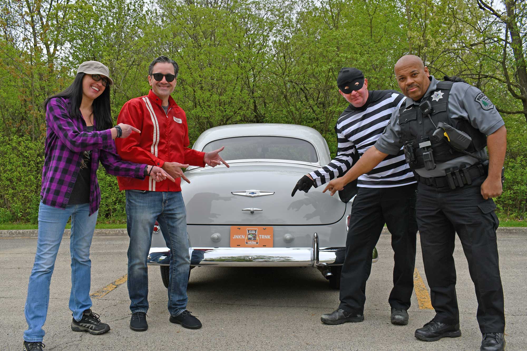 A man and woman pose with a police officer and a fake robber behind a 1949 Chevy.