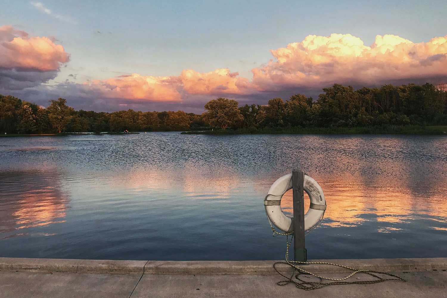 A life preserver in the foreground with a lake and a colorful pinkish sunrise in the background.