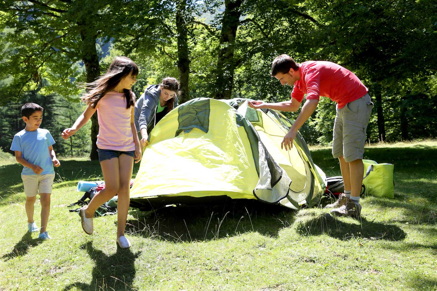 A man, a woman and two kids setting up a tent at a campsite