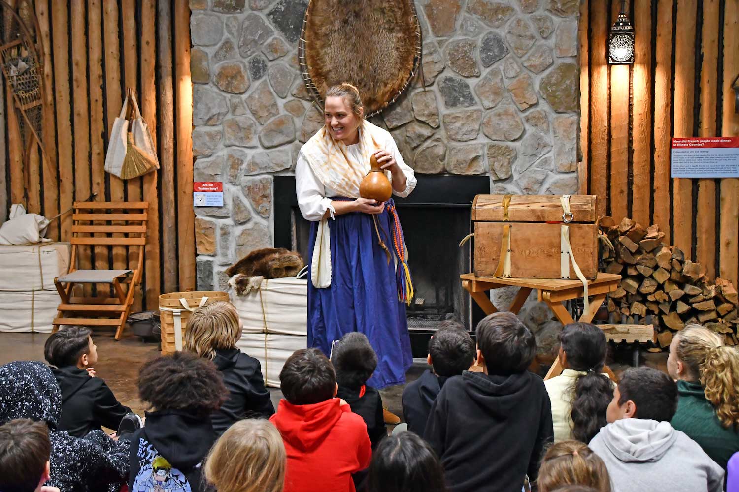 A person wearing traditional 18th-century clothing standing in front of a group of children sitting on the floor.