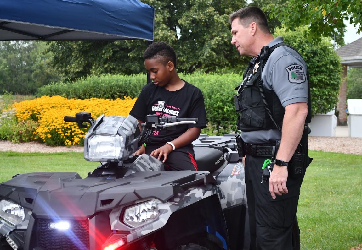 A police officer stands beside a young boy sitting on an ATV.