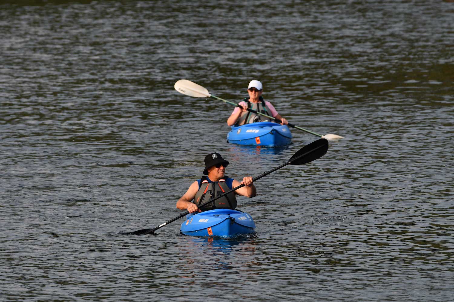 Two people paddling blue kayaks in a lake.