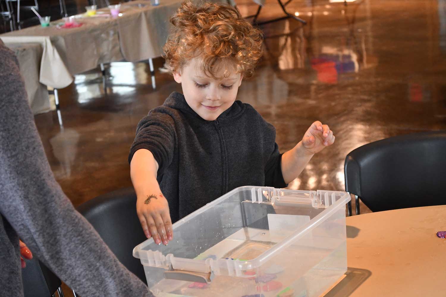A child playing with a bucket full on water while sitting inside at a table.