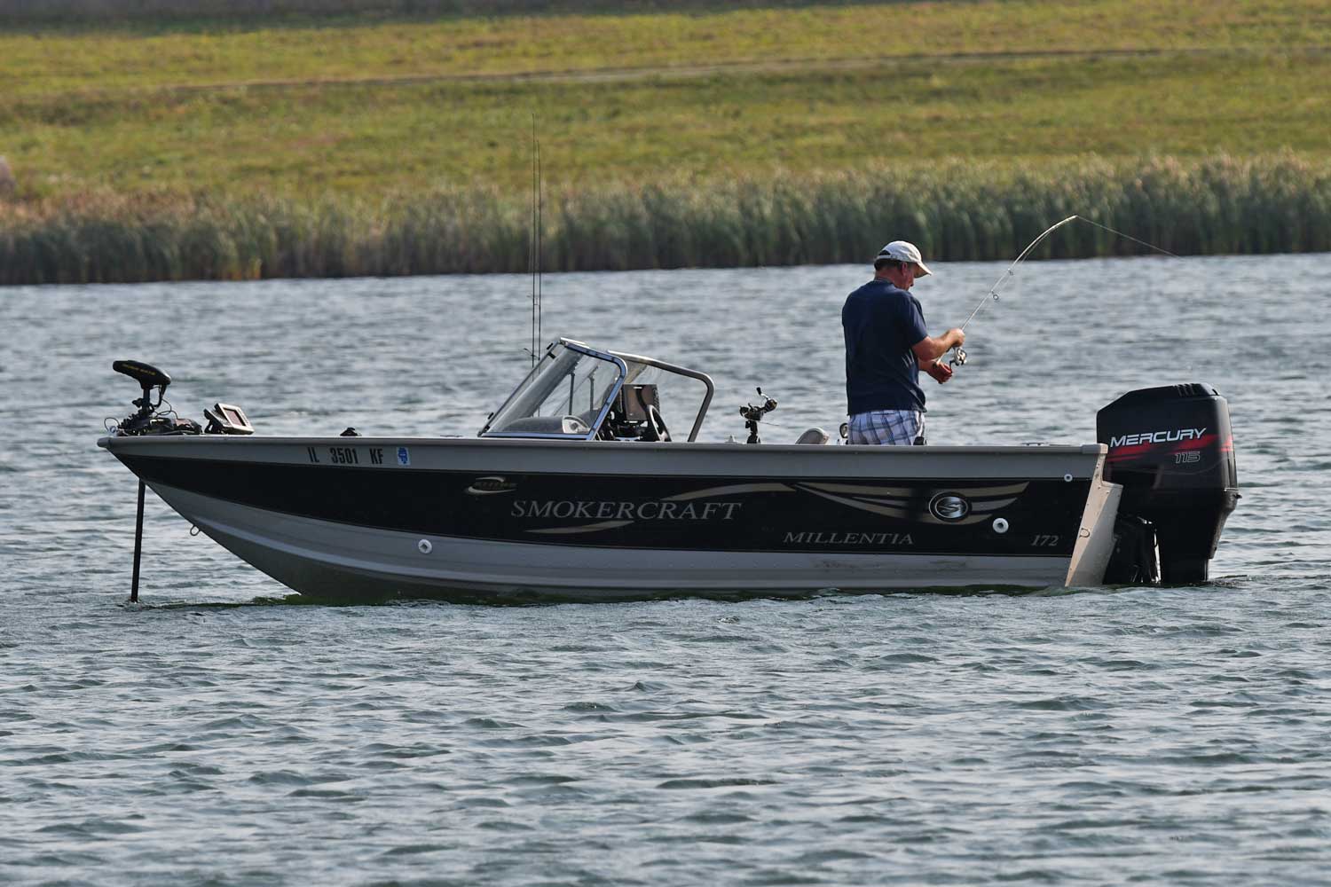 Person standing up in a boat while fishing with grasses in the background.