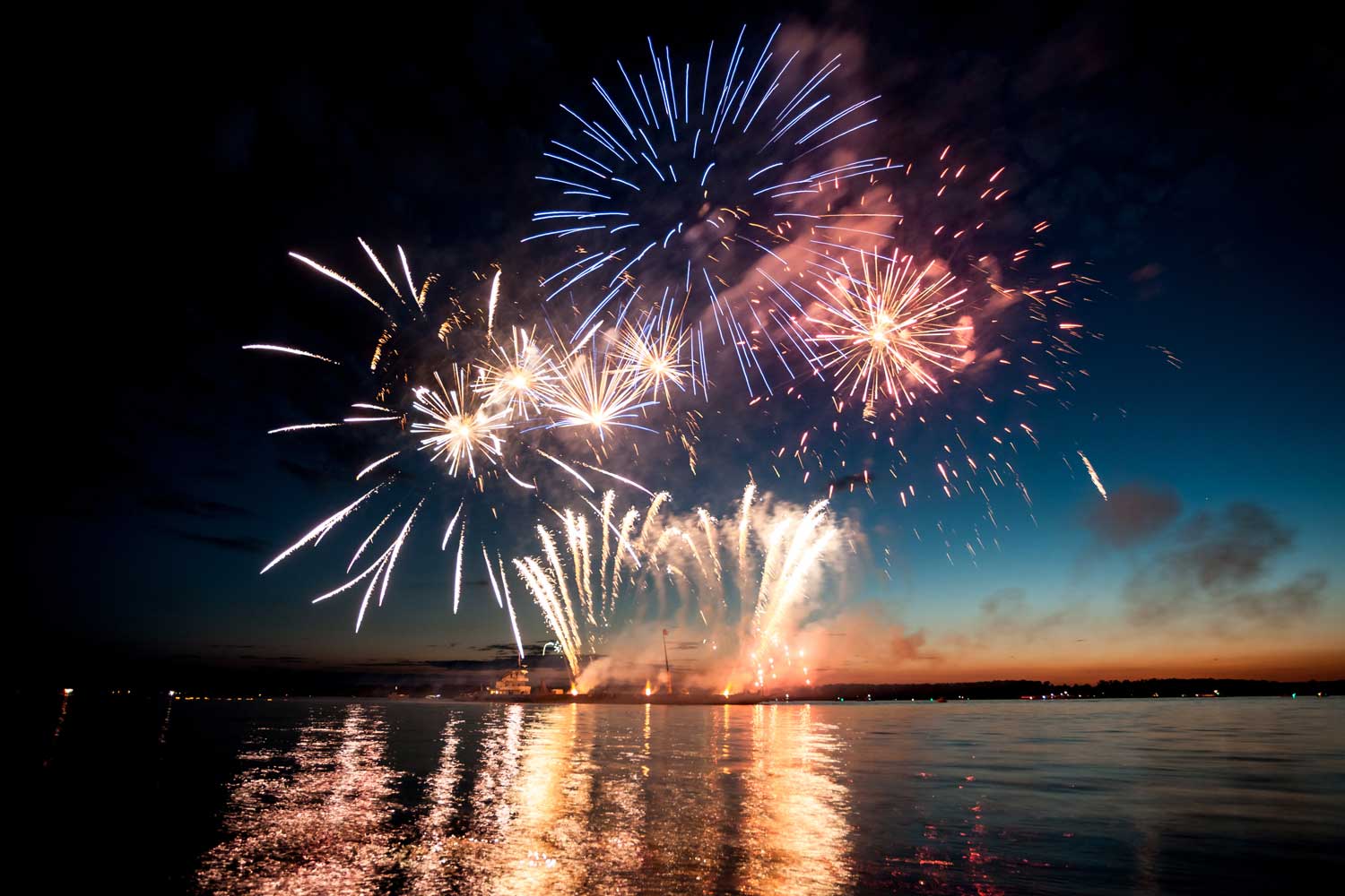 Fireworks lighting up the night sky over a lake.