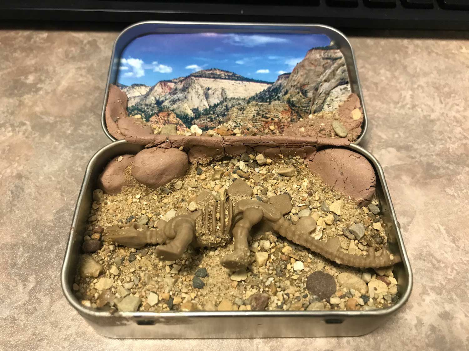 A diorama of a dinosaur habitat created in a small tin.