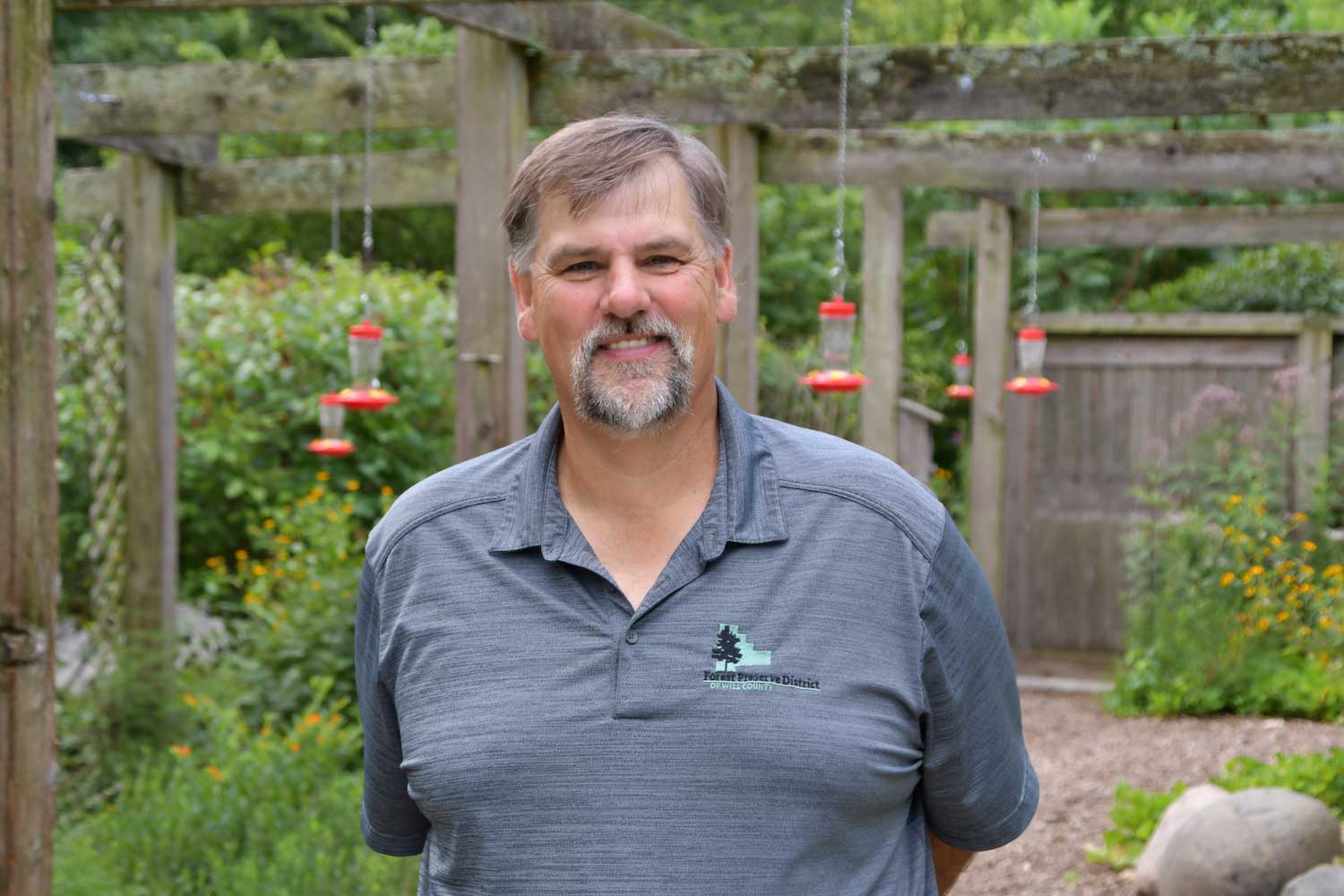 A man standing in front of a courtyard full of hanging hummingbird feeders.