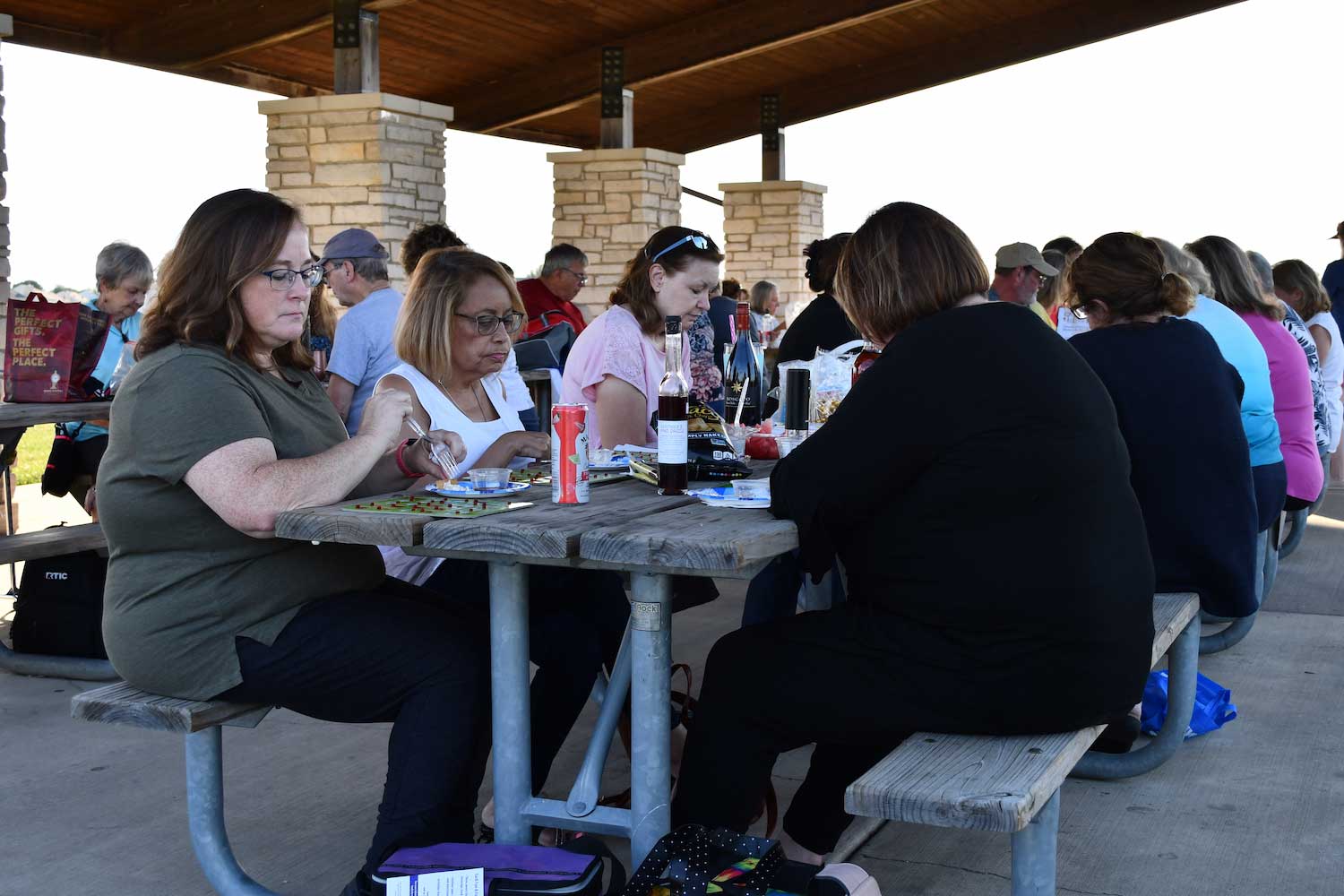 A group of people playing bingo at picnic tables in a shelter.